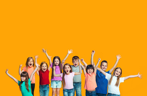 We won. Winning success happy teen girls and boys celebrating being a winner. Dynamic image of caucasian Children on orange studio background. Victory, delight concept. Human facial emotions concept. Trendy colors